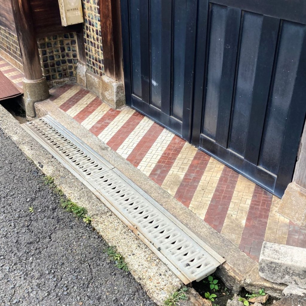 京都の軒先に残るレトロタイル床。赤・白・ベージュの縦ラインが並ぶデザインで、木製の引き戸と相まって味わい深い雰囲気を演出。