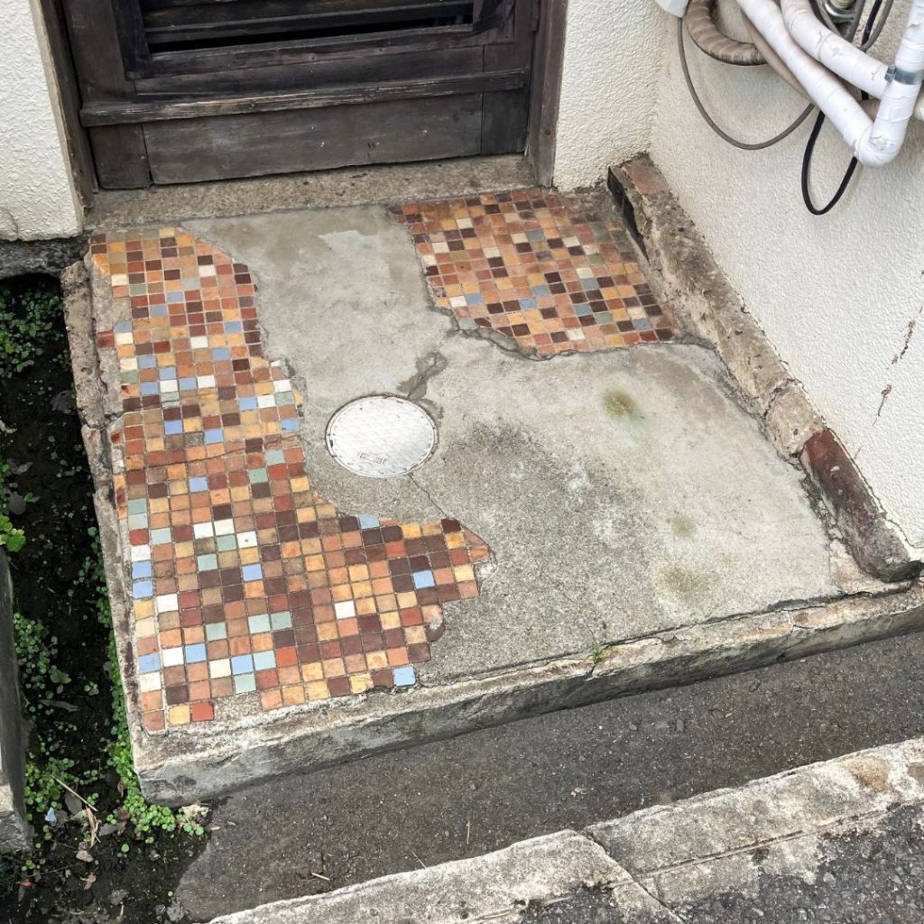 京都の民家の土間に残る、茶色や青などのモザイクタイルが部分的に剥がれた床の風景。