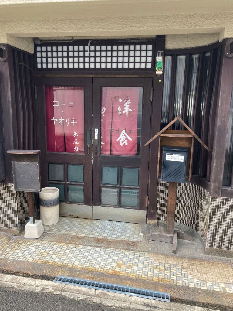 洋食店やをりきの木製ドアとタイル張りのアプローチ。クラシックな外観と矩形タイルの床が魅力的な佇まい。