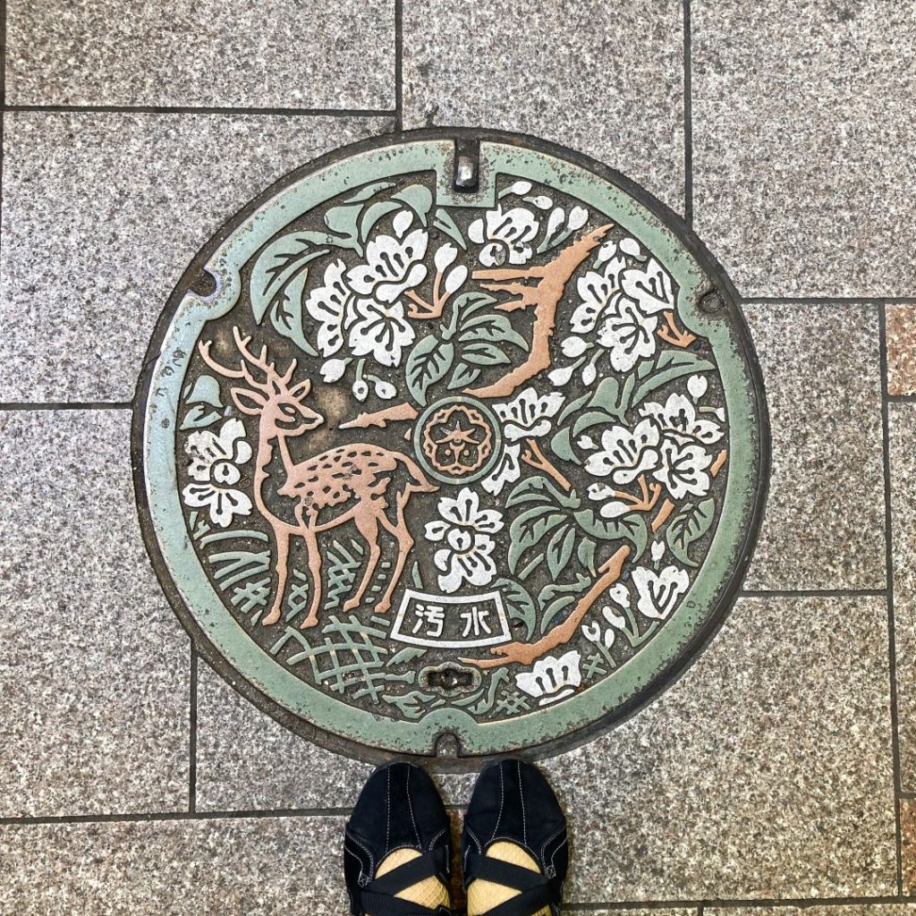 鹿と草花の意匠があしらわれた奈良のマンホール蓋。石畳の上に円形デザインが映える。