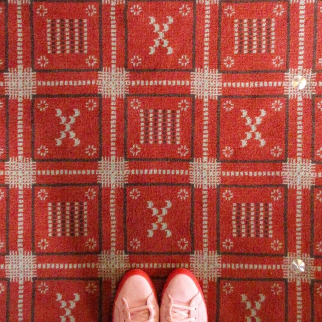 今井晶子の床旅で訪れた奈良ホテルのバーの床。赤を基調とした格子柄のクラシカルな絨毯に、繊細な模様が織り込まれている様子。