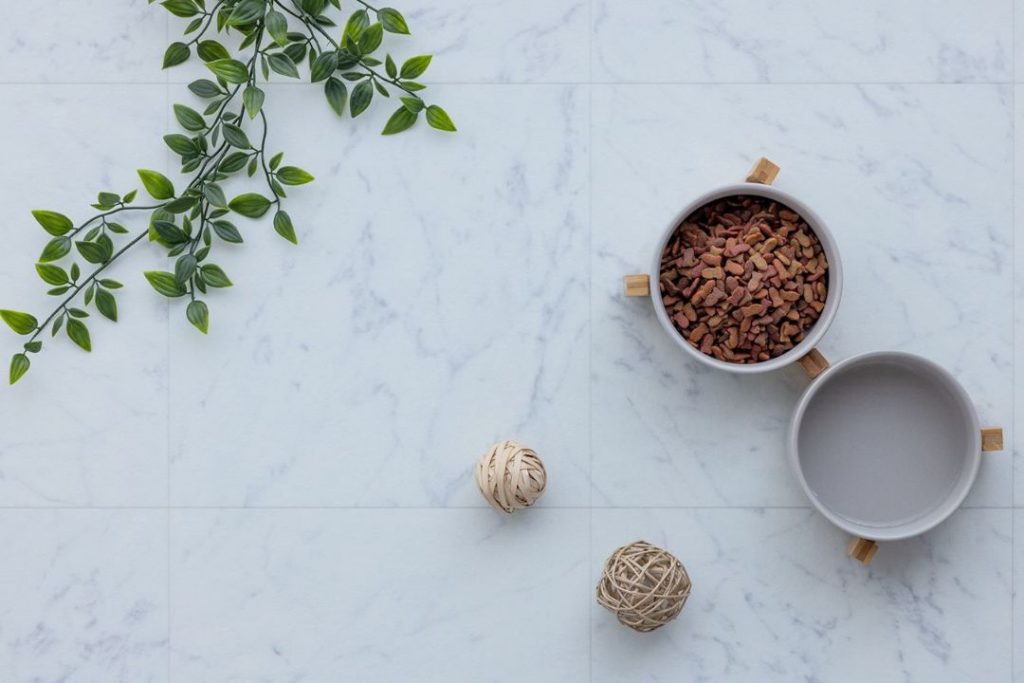 ラグリエのペットマット『大理石』白を基調としたマーブル調デザインの高機能クッションフロア。明るく清潔感のある床にエサ入れやインテリア小物が置かれたコーディネート例。