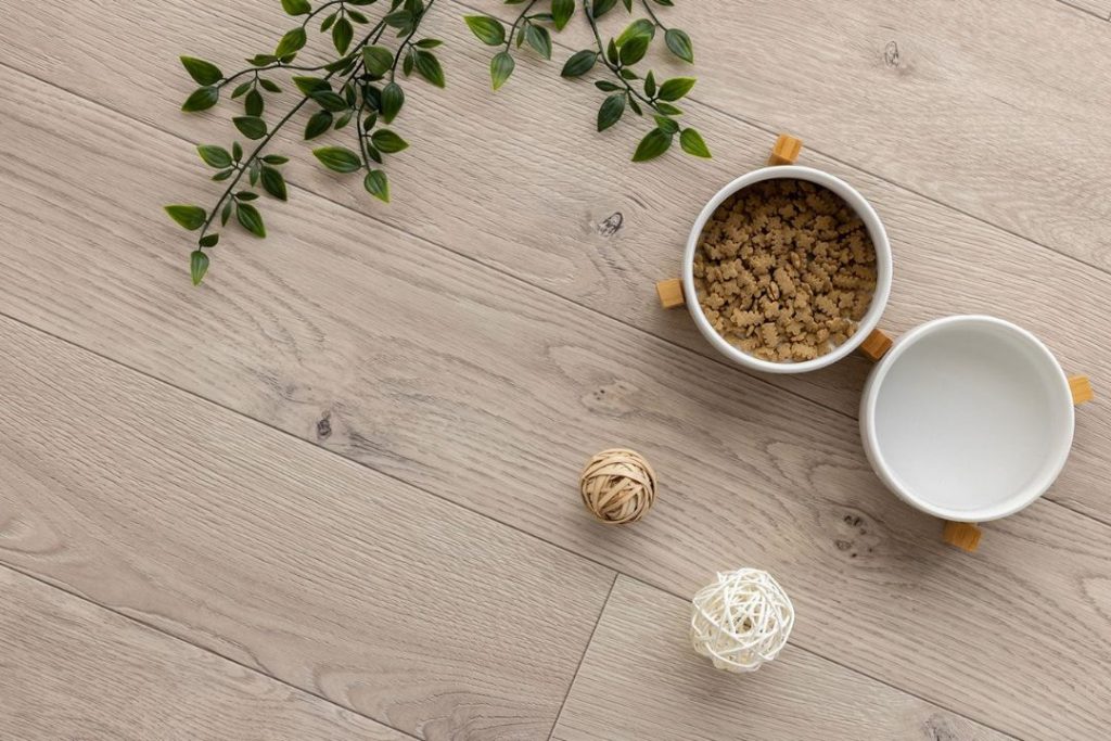 ラグリエのペットマット『ホワイトオーク』明るいベージュ系オーク調デザインの高機能クッションフロア。木目がはっきりとしたナチュラルな床にエサ入れやインテリア小物が置かれたコーディネート例。