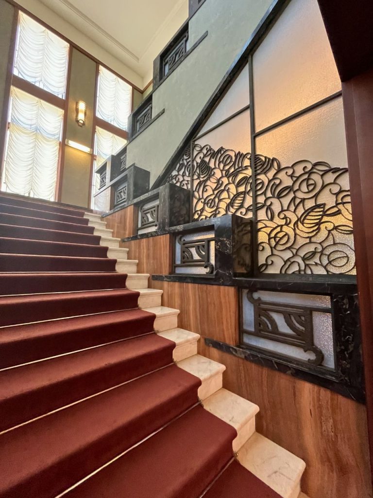 東京都庭園美術館の階段室。赤い絨毯の階段と、植物文様の装飾パネルが配されたアール・デコ様式の空間。