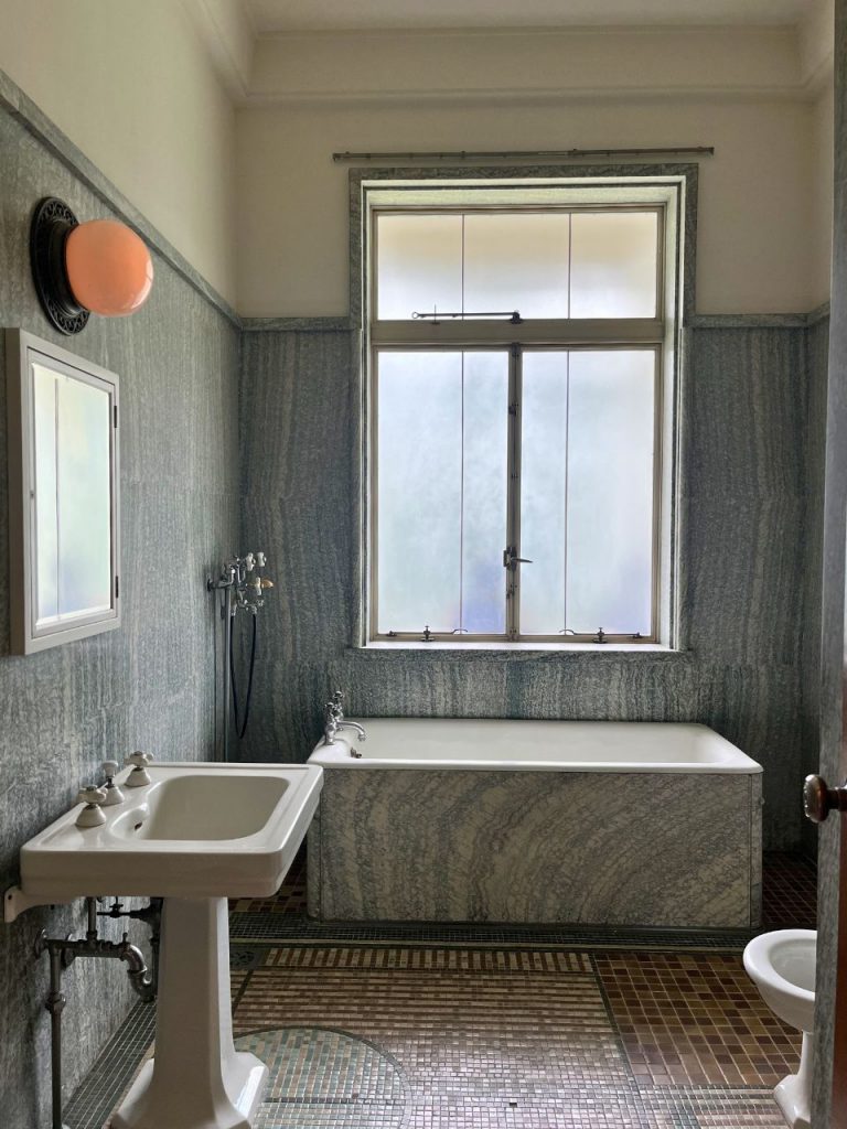 東京都庭園美術館（旧朝香宮邸）の浴室。大理石張りの壁と浴槽、モザイクタイル床、白い洗面台と窓が並ぶ室内