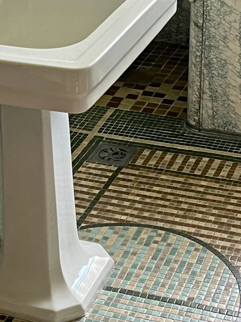 旧朝香宮邸の浴室床。排水口まわりに配された緑・ベージュ・茶のモザイクタイルと洗面台脚部