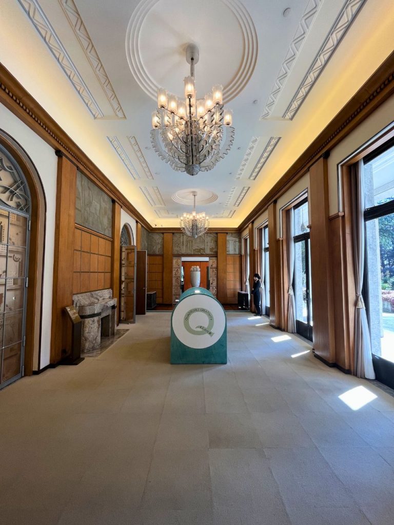 旧朝香宮邸の長い廊下空間。シャンデリアが連なる天井装飾と、木製パネル壁、石床が続く内部意匠