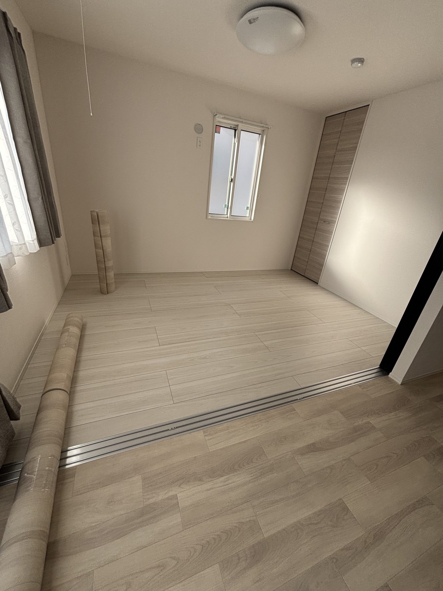 ラグリエのペットマット〈エッセンシャルバーチ〉を一部屋に敷いた施工途中の様子。隣の部屋にはまだ敷かれておらず、ロール状のマットが置かれている床DIYの途中段階。