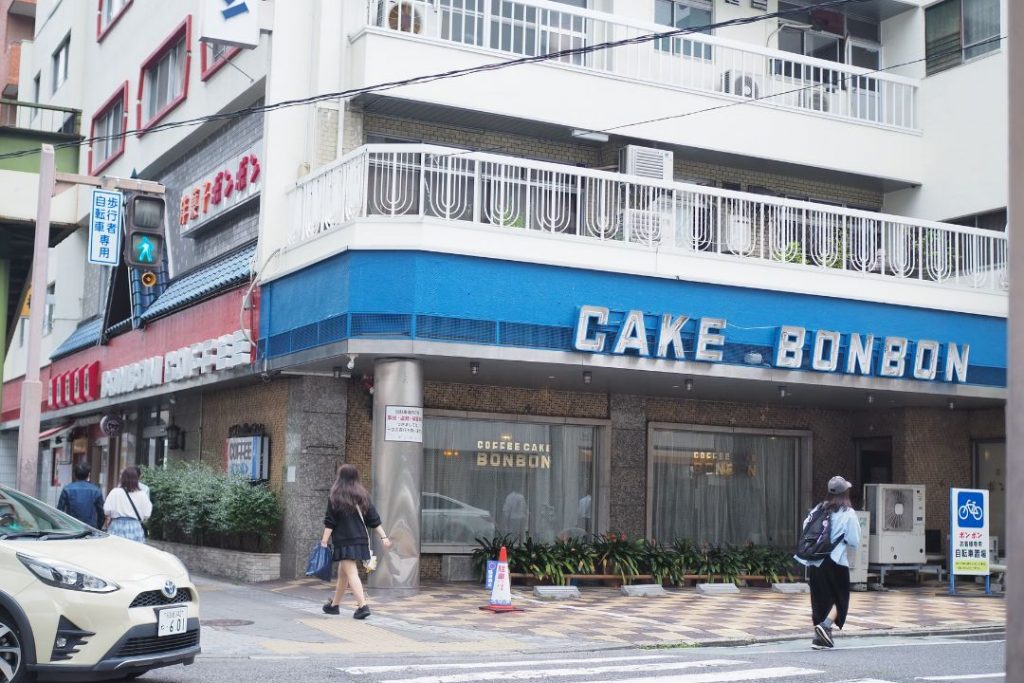 洋菓子・喫茶ボンボンの外観。角地に建つ店舗の青い看板や赤い文字の看板が見える、名古屋の老舗洋菓子店。