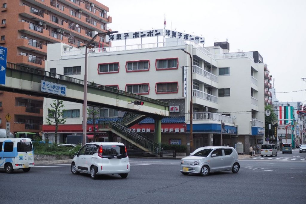 名古屋市東区にある洋菓子・喫茶ボンボン周辺の街並み。歩道橋や交差点越しに、ボンボンの建物と青い看板が見える。