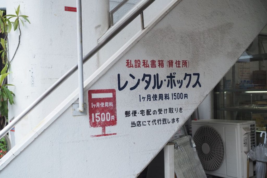 名古屋市東区の街歩きで見つけたレンタルボックスの壁面看板。階段下の壁に手描き風の文字で、私設私書箱や使用料の案内が書かれている。